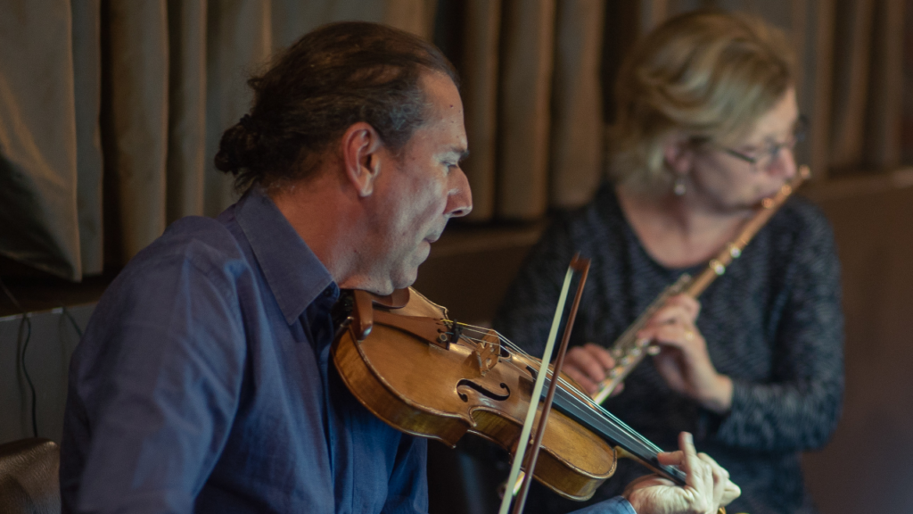 Rohan in focus playing the violin, Tracy playing flute